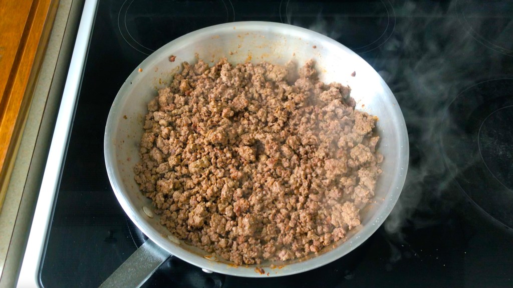 Ground lamb is browning in a pan over a high heat.