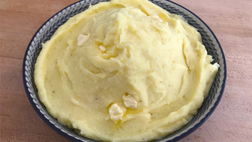 The final dish of mashed potatoes, in a serving bowl with a couple of extra pats of butter on top.