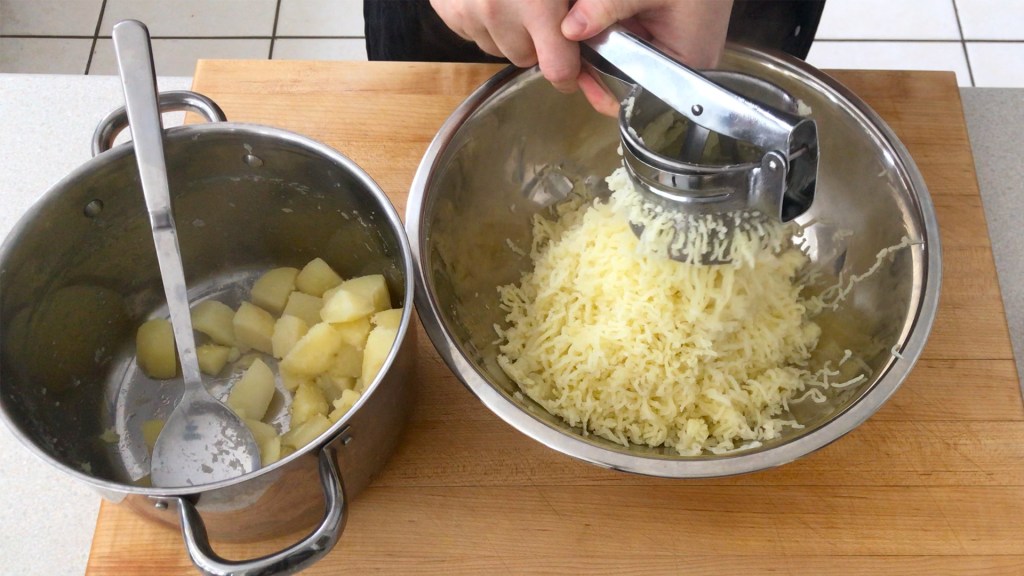 Passing the potatoes through a potato ricer to get a nice, smooth mash.