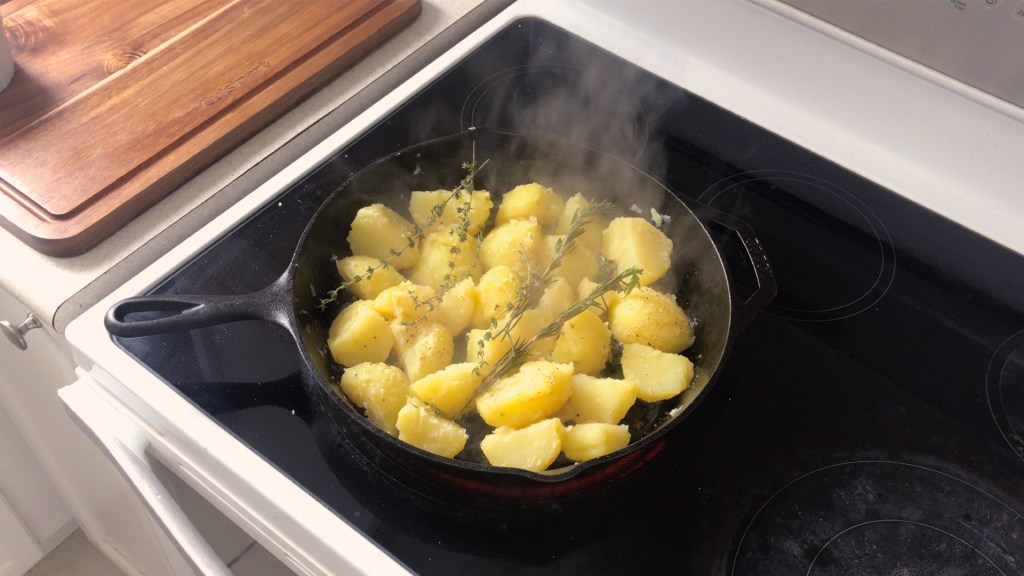 Potatoes and herbs in a cast iron pan on the stovetop, ready for the oven.
