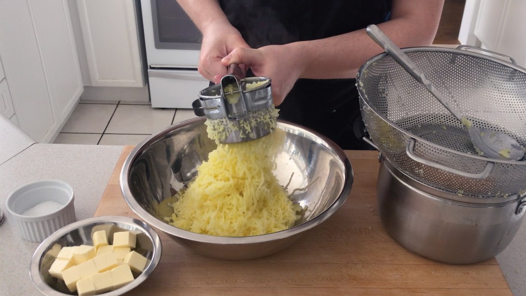 Pushing the boiled potatoes through a potato ricer to make a smooth mash.