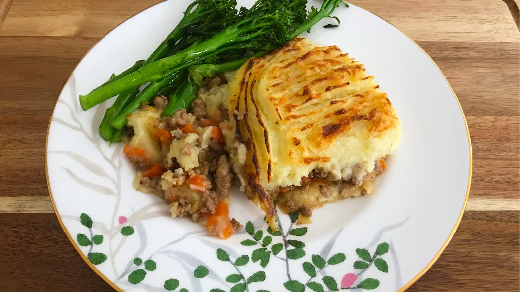 A portion of shepherd's pie on a plate, with steamed broccolini on the side. Delicious!